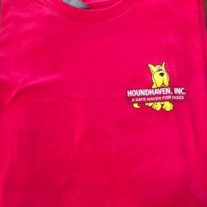 This is a picture of the top half of a fuchsia (dark pink) crew neck t-shirt. On the right side is a small cartoon of a sitting yellow Great Dane. On top of the Dane's body are two rows of white writing. The first row in bold and all capitals says HOUNDHAVEN, INC. The second row in a smaller font size in all caps says,"A SAFE HAVEN FOR DOGS", You can see the Dane's paws and bottom half of the tail peeking out from the last line of writing.