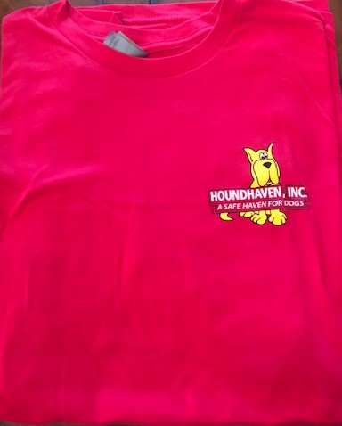 This is a picture of the top half of a fuchsia (dark pink) crew neck t-shirt. On the right side is a small cartoon of a sitting yellow Great Dane. On top of the Dane's body are two rows of white writing. The first row in bold and all capitals says HOUNDHAVEN, INC. The second row in a smaller font size in all caps says,"A SAFE HAVEN FOR DOGS", You can see the Dane's paws and bottom half of the tail peeking out from the last line of writing.