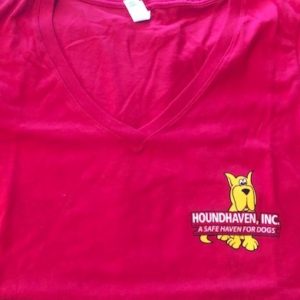This is a picture of the top half of a fuchsia (dark pink) v-neck t-shirt. On the right side is a small cartoon of a sitting yellow Great Dane. On top of the Dane's body are two rows of white writing. The first row in bold and all capitals says HOUNDHAVEN, INC. The second row in a smaller font size in all caps says, "A SAFE HAVEN FOR DOGS", You can see the Dane's paws and bottom half of the tail peeking out from the last line of writing.