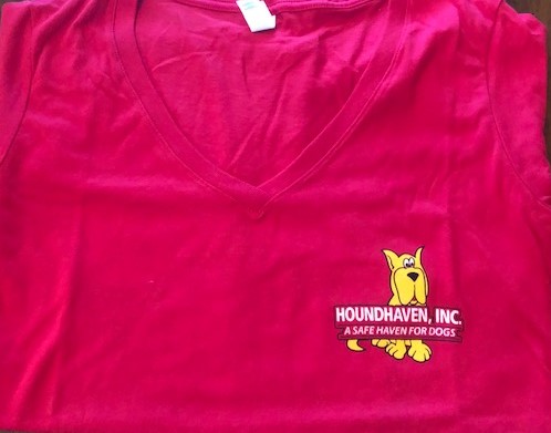 This is a picture of the top half of a fuchsia (dark pink) v-neck t-shirt. On the right side is a small cartoon of a sitting yellow Great Dane. On top of the Dane's body are two rows of white writing. The first row in bold and all capitals says HOUNDHAVEN, INC. The second row in a smaller font size in all caps says, "A SAFE HAVEN FOR DOGS", You can see the Dane's paws and bottom half of the tail peeking out from the last line of writing.